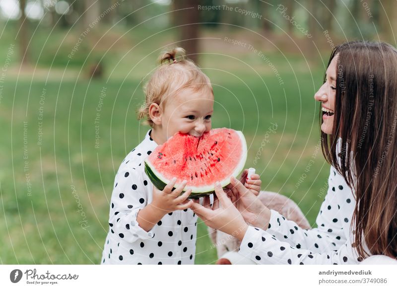 glückliche Mutter und Tochter essen Wassermelone im Sommerpark. Glücklich lächelnde Familie isst Wassermelone im Park. Mutter und Tochter verbringen Zeit miteinander. Diät, Vitamine, Konzept für gesunde Ernährung. selektiver Fokus