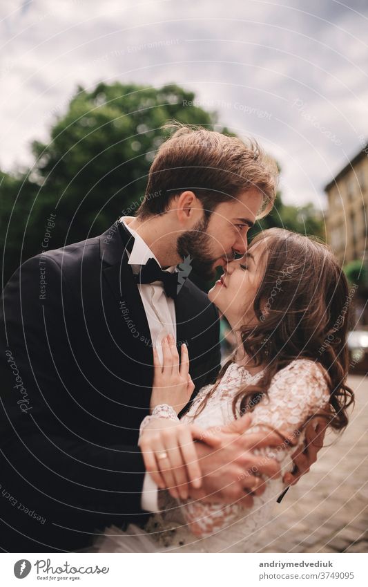 Glückliches frisch verheiratetes Paar umarmt und küsst sich in der Straße der alten europäischen Stadt, wunderschöne Braut im weißen Brautkleid zusammen mit hübschem Bräutigam. Hochzeitstag