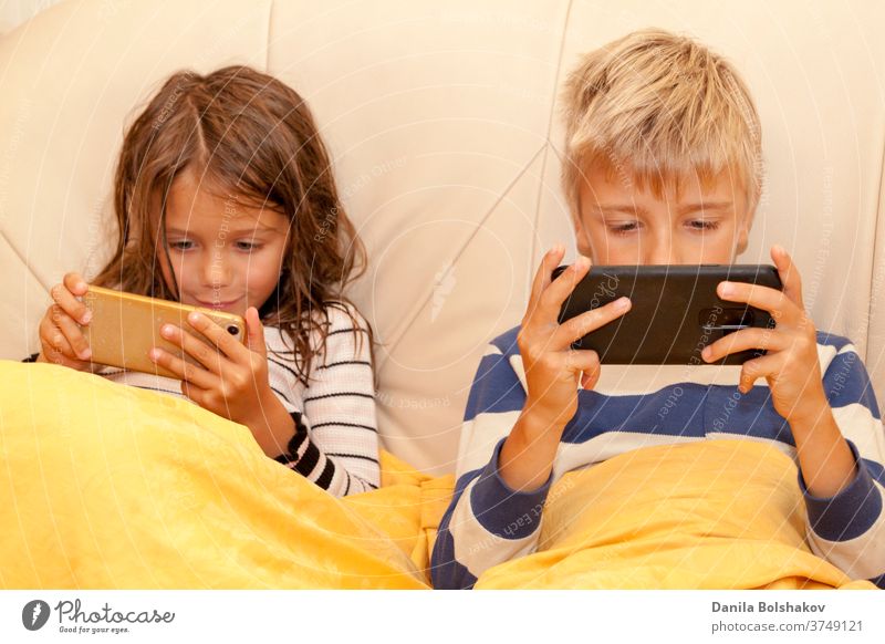 Kleines Mädchen und Junge spielen ein Spiel oder sehen sich etwas auf einem Smartphone an Cartoons Handy aussruhen Karikaturen anschauen Surfen im Netz