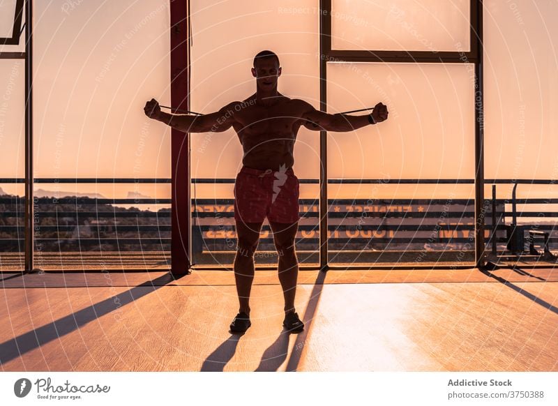 Sportlicher Mann macht Übungen mit Widerstandsband elastisch Band widersetzen stark Dehnung Pumpe Muskel Fitnessstudio männlich Sonnenuntergang Sonnenlicht