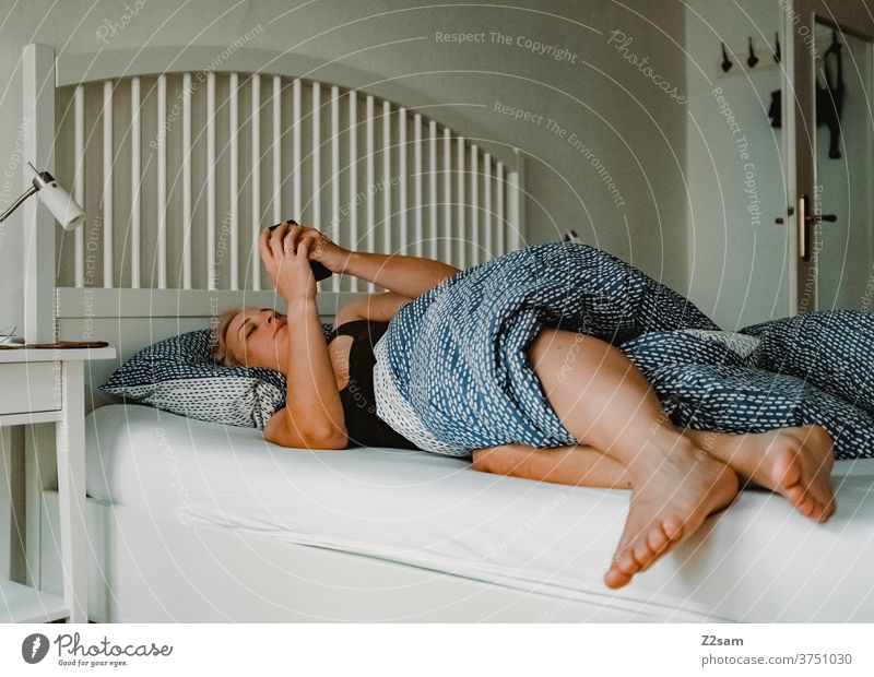 Junge Frau im Bett mit dem Smarphone zuhause erholung entspannung wohnen gemütlich fenster licht altbau junge frau blond lange haare schön hübsch liegen handy