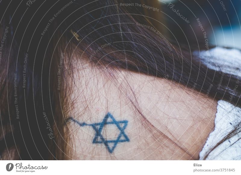 Der Davidstern, Symbol des Judentums, als Tattoo auf dem Rücken einer Frau mit langen braunen Haaren Religion religiös Glaube gläubig Jugenich Junge Frau