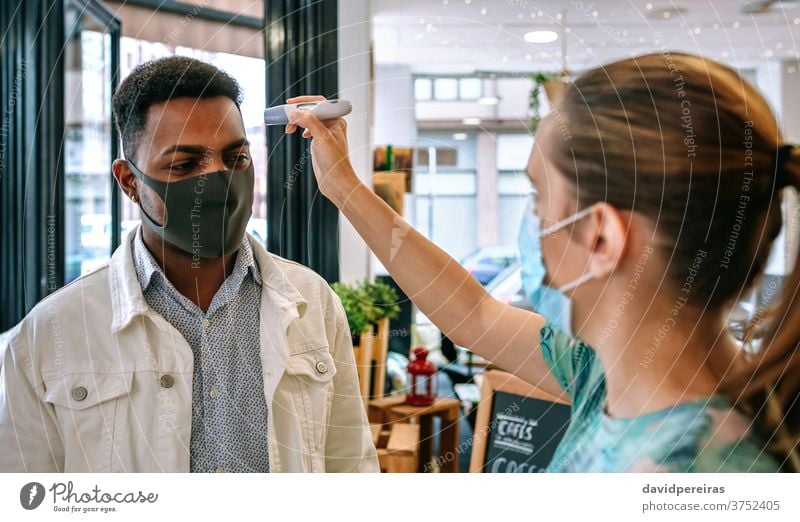 Geschäftsinhaber überprüft Kunden auf Fieber Frau Überprüfung Temperatur Mann Infrarot-Thermometer covid-19 Coronavirus Arbeitnehmer Gesichtsmaske Blick