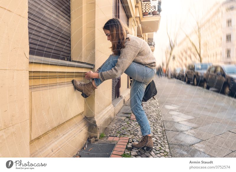junge Frau bindet ihren Schuh auf der Straße Porträt im Freien Straßenbelag Autos Großstadt Stadt urban hockend Schuhe Sommer schön konzentriert Tasche Wand