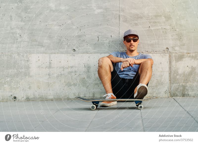 Stilvoller Mann mit Skateboard in der Stadt Skater urban Gebäude Hobby Fähigkeit fettarm Wand männlich Outfit selbstbewusst trendy Straße modern jung Großstadt