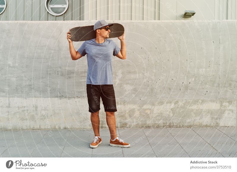 Selbstbewusster Mann mit Skateboard in der Nähe des Gebäudes Großstadt Skater Bestimmen Sie Stil Hobby trendy urban Straße männlich Sonnenbrille Outfit modern