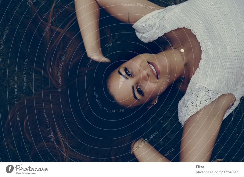 Junge dunkelhaarige Frau liegt auf dem Boden mit den Händen in den Haaren und blickt strahlend nach oben in die Kamera junge Frau braunhaarig Beautyfotografie