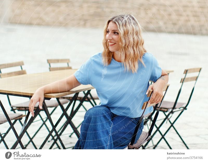 Junge Frauen in T-Shirt und Jeans sitzen in einem Straßencafé jung Mädchen anhaben Attrappe Jeanshose sitzt Café Tisch Rundhals Bekleidungsmockup lässig Sitz