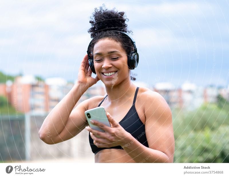 Zufriedene Sportlerin, die mit Kopfhörern Musik hört zuhören Training genießen Athlet passen Freude Smartphone Frau ethnisch schwarz BH Großstadt Drahtlos