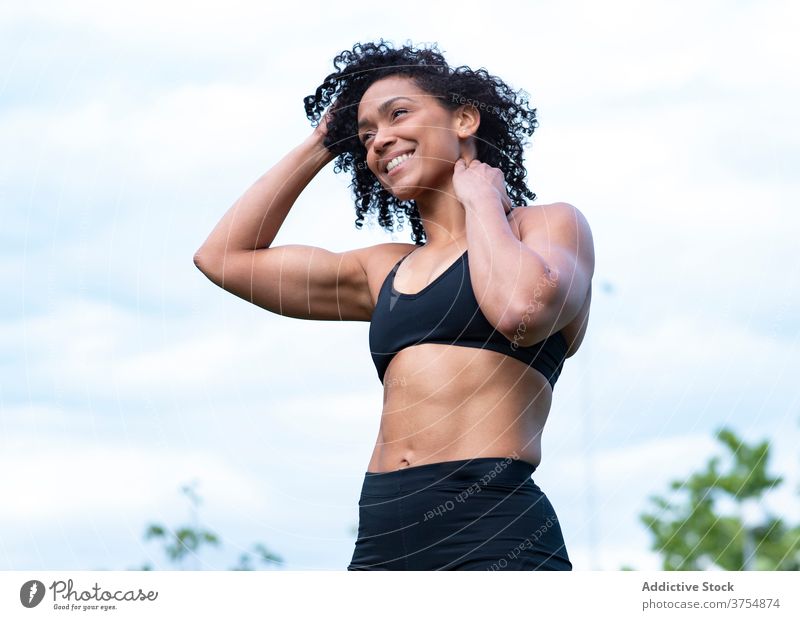 Lächelnde schwarze Sportlerin beim Aufwärmen im Park muskulös Training Frau Athlet stark Dehnung Sportbekleidung ethnisch Afroamerikaner Gesundheit passen Übung