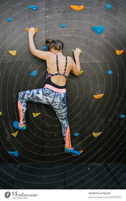 Mutiges Mädchen klettert Wand in der Turnhalle Aufstieg Kind Felsbrocken Fitnessstudio künstlich Felsen Griff Training Gleichgewicht Halt furchtlos üben Übung