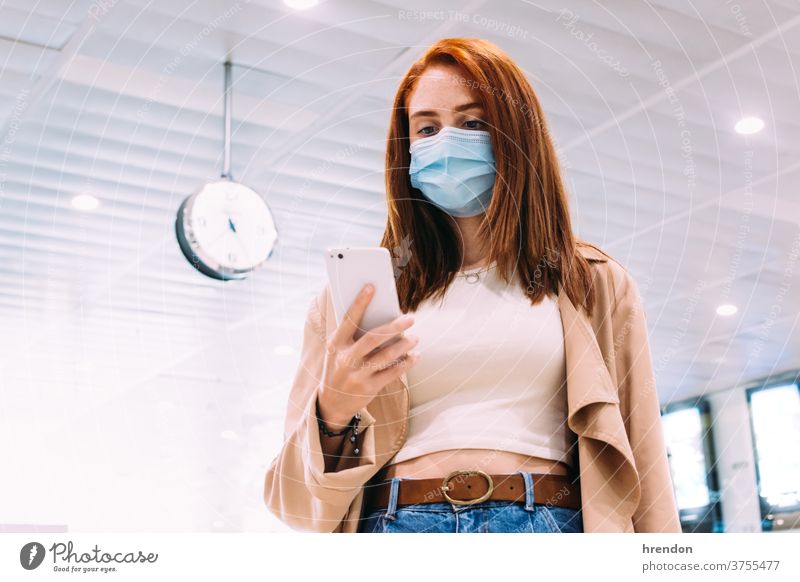 Frau mit Maske, die ihr Smartphone am Bahnhof benutzt Öffentlich Reise Tourist Ausflug Zug reisend Wirtschaft Virus Coronavirus Seuche Pandemie Mundschutz