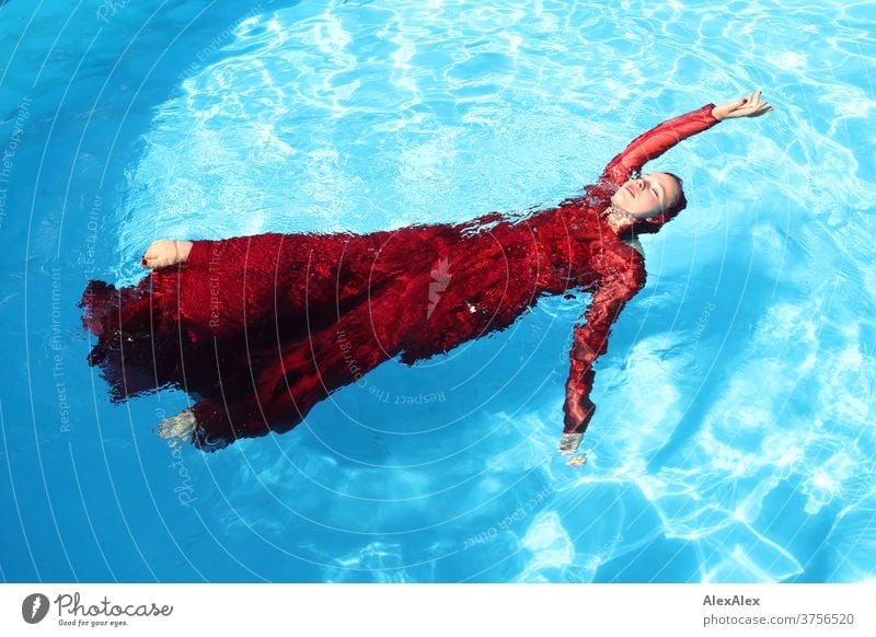 Junge Frau in rotem Ballkleid liegt mit ausgestrecktem Arm in einem Swimmingpool junge Frau Mädchen schön anmutig sportlich schwimmen Sonnenlicht Sommer Pool