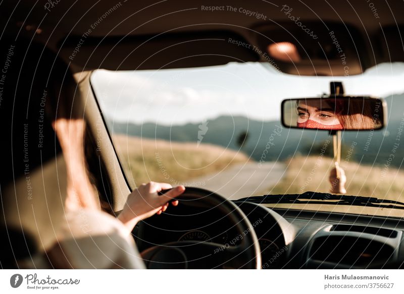 Frau mit Maske fährt Auto, Gesicht im Rückspiegel, reist in der 19