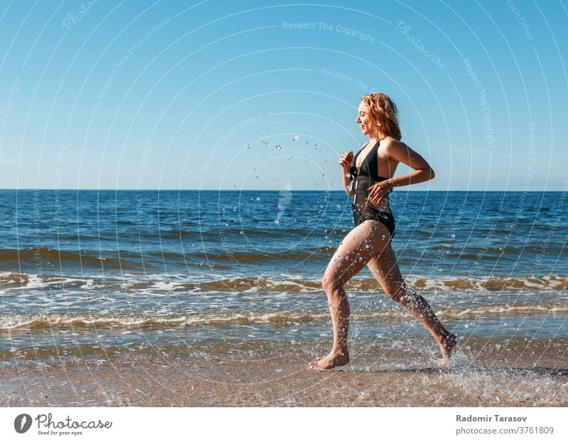 ein junges blondes Mädchen in einem schwarzen Badeanzug läuft am Sand des Meeresufers entlang Schönheit Kaukasier Körper schön Model Frau Wasser Person Sommer