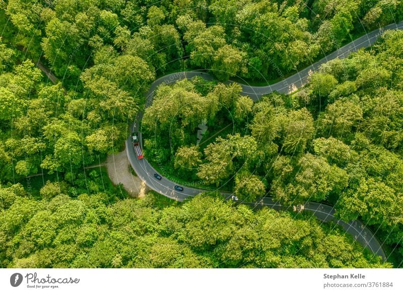 Luftaufnahme eines grünen Waldes mit einem Traktor auf seiner Durchfahrtsstraße, der eine Reihe von Autos hinter sich abbremst - Stau an einem schönen Reisetag