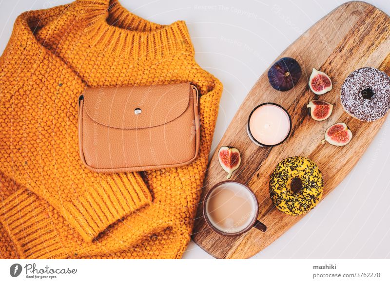 gemütliche Herbstmorgen-Flachlegerkomposition mit warmem Pullover, Tasse Kaffee, süßem Donut zum Frühstück und Modehandtasche fallen Winter Morgen