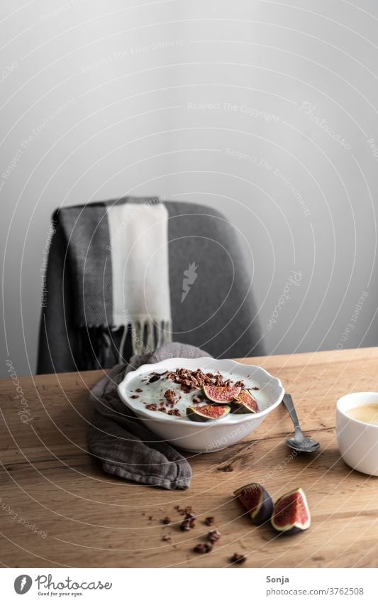 Frühstückstisch mit Granola, Joghurt und frischen Feigen und eine Sessellehne. Weiße Wand, gesunde Ernährung. Müsli Kaffee Tasse Löffel Innenaufnahme Farbfoto