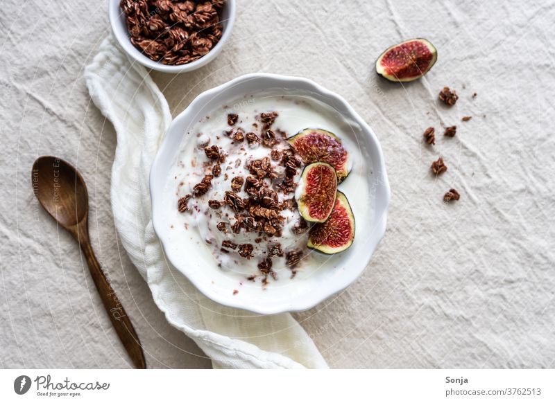 Granola mit Joghurt und frischen Feigen in einer Schüssel auf einem beigen Leinentuch. Drausicht, gesundes Frühstück. Löffel Frucht rustikal