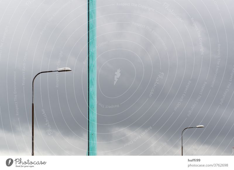 zwei Lampen und ein türkiser Pfahl vor grauem Himmel - ein Sturm kommt auf Straßenlampe Peitschenlampen minimalistisch Farbfoto stürmisch stürmische zeiten