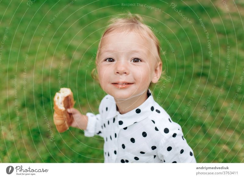 Süßes und lustiges kleines Mädchen mit Brötchen in der Hand und lächelnd vor einem diffusen grünen Grashintergrund. selektiver Fokus niedlich Kind Freude Spaß
