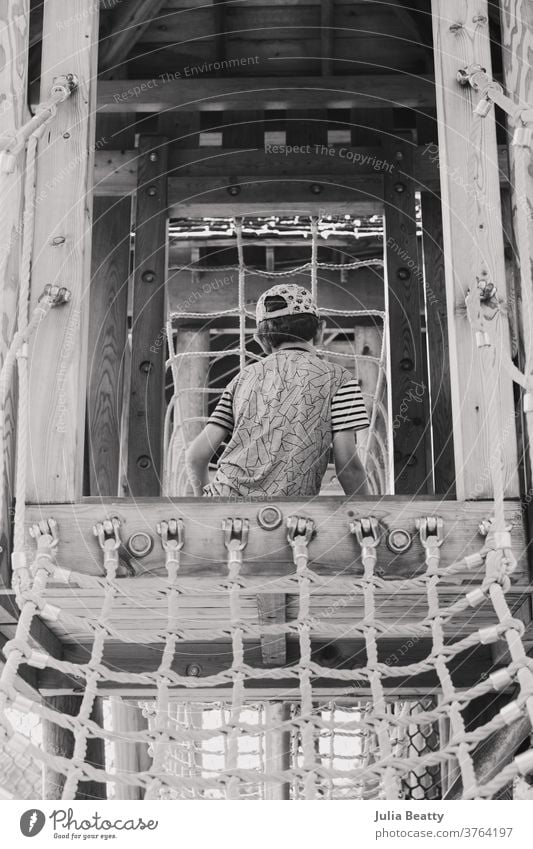 Junge auf einem Spielplatz mit Holzkonstruktion und Seilnetz Spielset Klettern Aufstieg erkunden Kind Seile Strickleiter Netz hölzern Schulpause spielen Spielen
