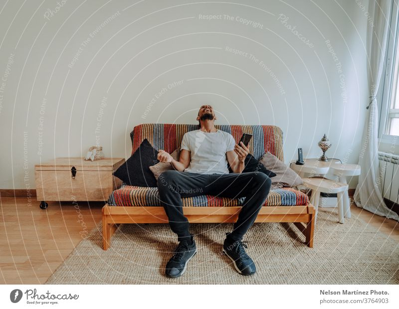 Ein spanischer Mann sitzt auf der Couch. Er lacht mit seinem Smartphone in der Hand. 1 Freiheit Erwachsener Blick Freizeitkleidung Lachen Lifestyle Feiertag