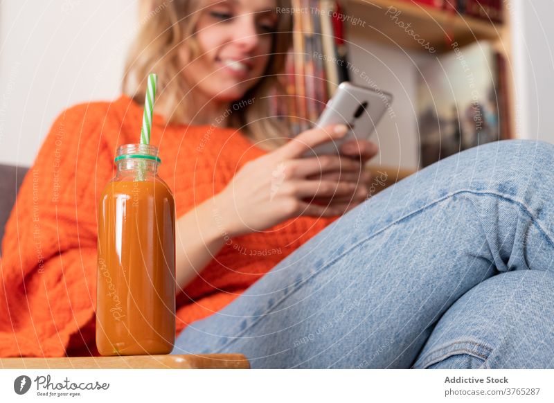 Frau mit Smartphone im Zimmer mit Smoothie-Getränk Entzug trinken frisch benutzend geschmackvoll Ernährung Sofa Browsen Funktelefon Gesundheit Saft Glas Flasche