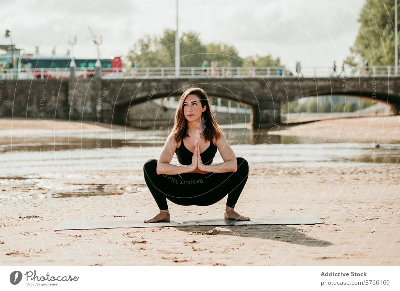 Schlanke Frau in Garland-Pose beim Yoga am Strand Girlandenpose malasaña üben Gleichgewicht Sommer Asana Ufer Unterlage ruhig Fluss Gesundheit schlank Harmonie