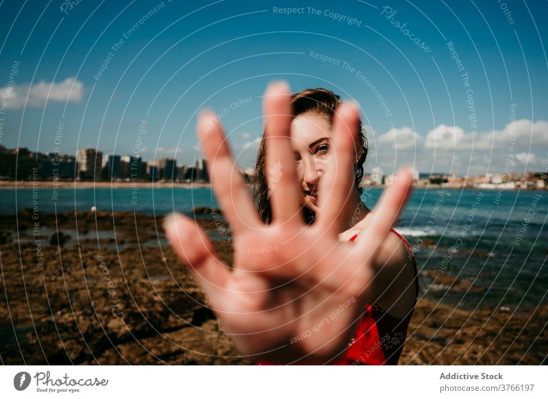 Lächelnde Frau zeigt Hände zur Kamera Anmut sich[Akk] melden Hand gestikulieren Meeresufer charmant Inhalt zeigen manifestieren sonnig Sommer Feiertag Küste