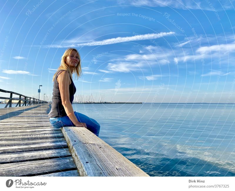 Blonde Frau sitzt auf einer Seebrücke an der Ostseeküste 45-60 Jahre schön blond Porträt anschauend Blick Mensch Erwachsene feminin Blick in die Kamera