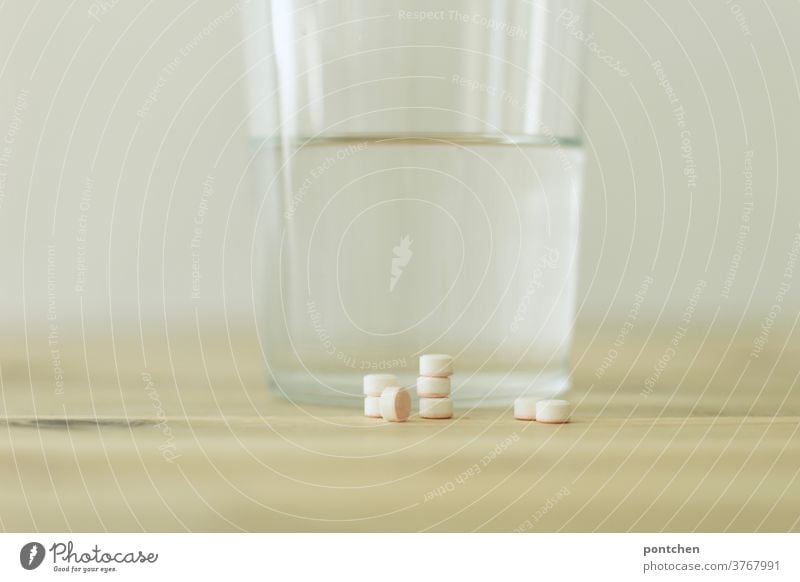 Mehrere Tabletten aufgestapelt liegen vor einem Trinkglas gefüllt mit Wasser auf einem Tisch. Krankheit, Medikamente. Tablettensucht. medizin wasserglas