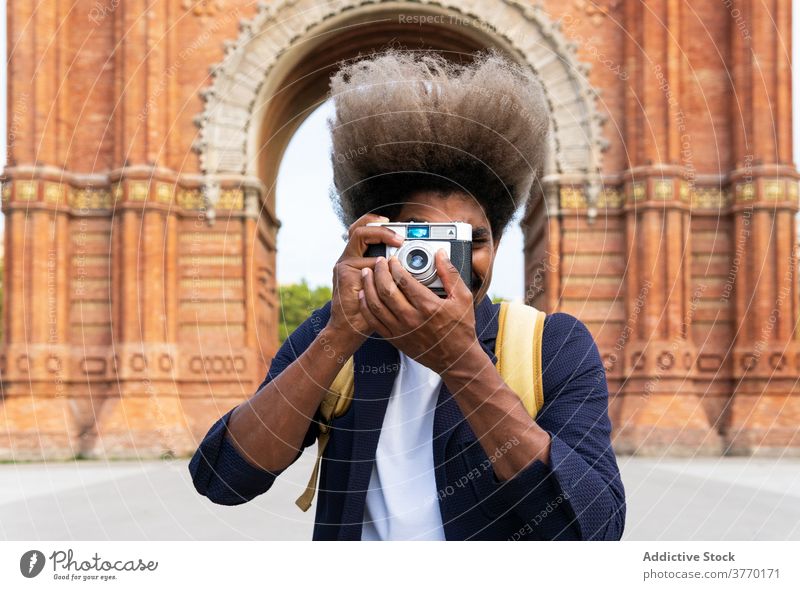 Schwarzer Mann, der ein Foto macht, während er mit der Kamera in die Kamera schaut Journalist Linse Bild Brühe modisch trendy Hobby Fotografie stylisch