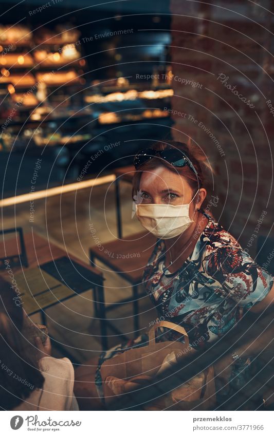 Junge Frau sitzt im Café an der Ladenfront im Stadtzentrum und trägt die Gesichtsmaske, um eine Virusinfektion zu vermeiden Kaukasier Gespräch covid-19
