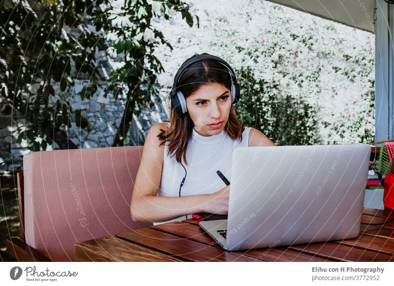 junge Lateinamerikanerin sitzt allein im Heimbüro, arbeitet am Laptop und hört Musik über Kopfhörer, mexikanisches Mädchen in Mexiko arbeitet zu Hause Drahtlos