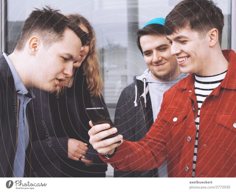 junger Mann, der einer Gruppe von Freunden etwas Lustiges auf dem Smartphone zeigt Teenager Menschengruppe echte Menschen Lifestyle zeigen Handy lustig zusammen