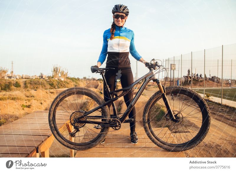 Sportliche junge Frau in Helm mit Fahrrad schaut in die Kamera Schutzhelm Lächeln Berge u. Gebirge Testversion Radfahrer Trick Sportlerin Radfahren