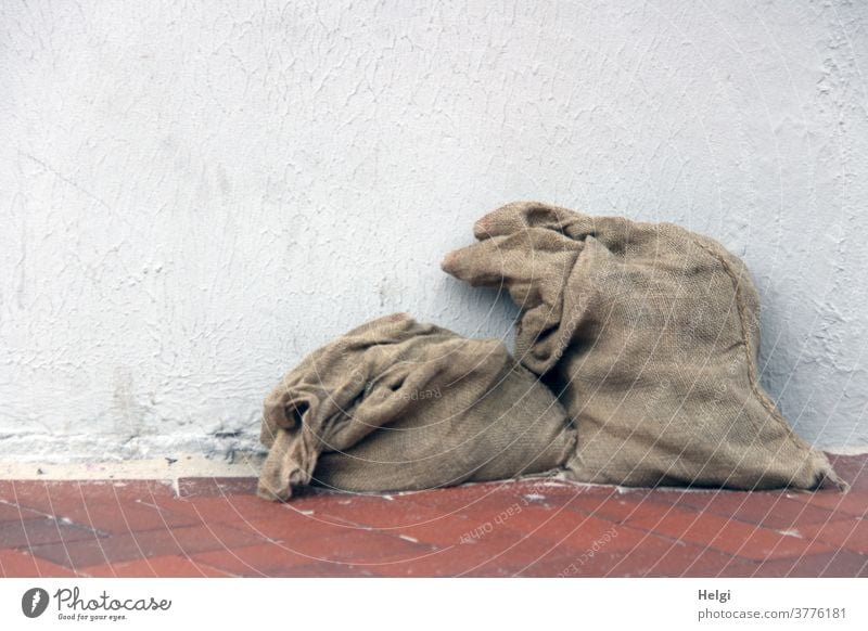 AST ;-) - zwei alte zum Teil gefüllte Jutesäcke auf rotem Klinkerboden lehnen an einer weißen Wand Sack Jutesack 2 stehen braun grau Farbfoto Menschenleer