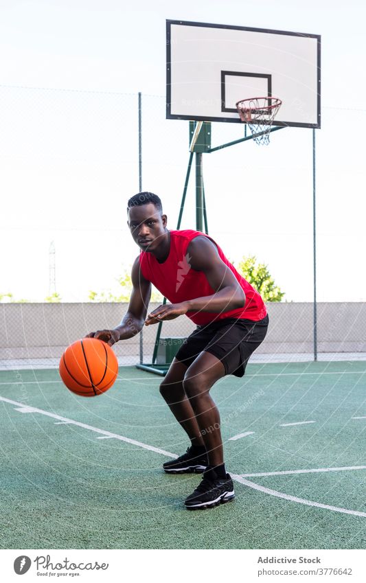 Konzentrierter schwarzer Mann spielt Basketball auf dem Platz Spieler spielen Ball Sportpark Spielplatz ernst Taktik Fokus männlich Afroamerikaner ethnisch