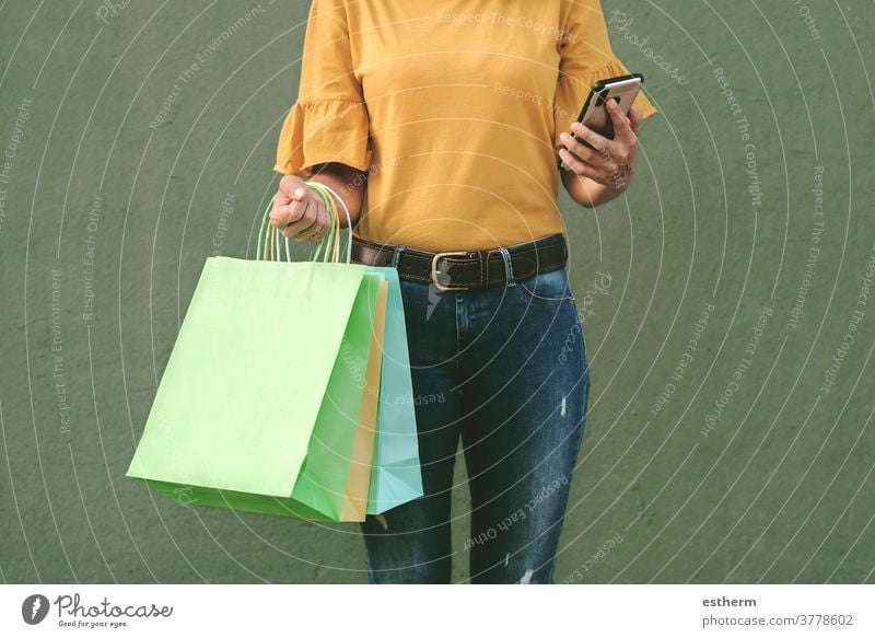 Frau, die eine Einkaufstasche und ein Smartphone in der Hand hält Junge Frau kaufen Frau beim Einkaufen Einkaufstaschen Werkstatt Käufer Lächeln Mädchen Spaß