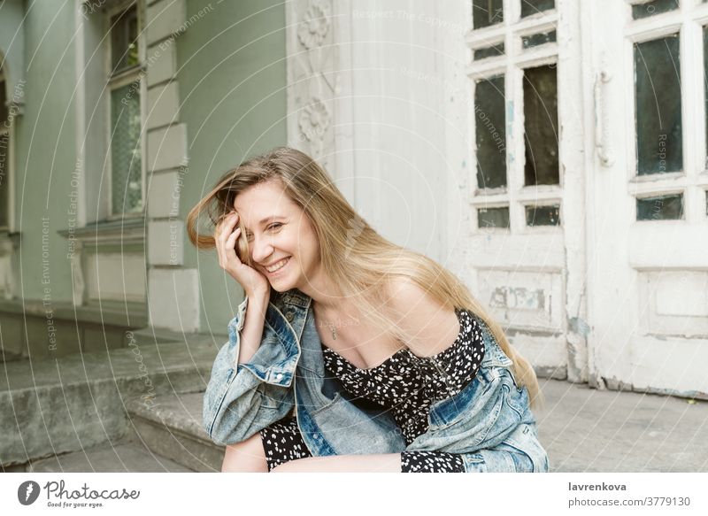Porträt einer lachenden blonden Frau in Kleid und Jeansjacke, die im Freien sitzt Lächeln Menschen Lifestyle Glück Mädchen attraktiv freudig Kaukasier