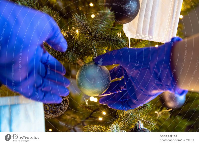 Person, die einen schönen Weihnachtsbaum mit Schutzhandschuhen für Covid-19 schmückt, Konzept für Coronavirus und Weihnachtsfeiertag erhängen Glück zu feiern