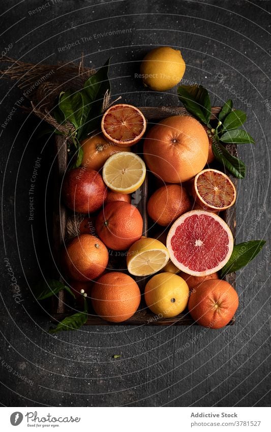 Assortierte Zitrusfrüchte auf schwarzem Tisch angeordnet Frucht verschiedene reif frisch Zitrone orange Grapefruit Mandarine hölzern Tablett grün Blatt Ordnung