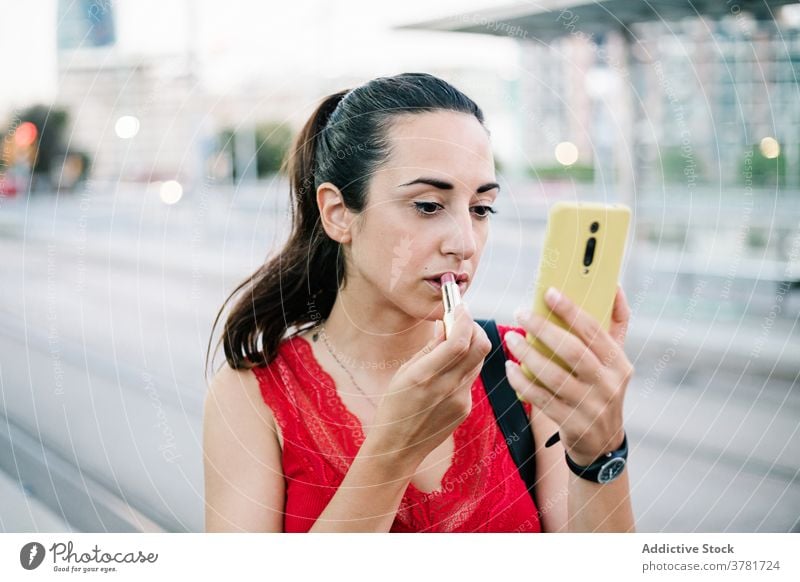 Junge Frau mit Smartphone trägt Lippenstift auf der Straße auf Make-up bewerben Schönheit Kosmetik Mobile urban modern Funktelefon Telefon Gerät Apparatur jung