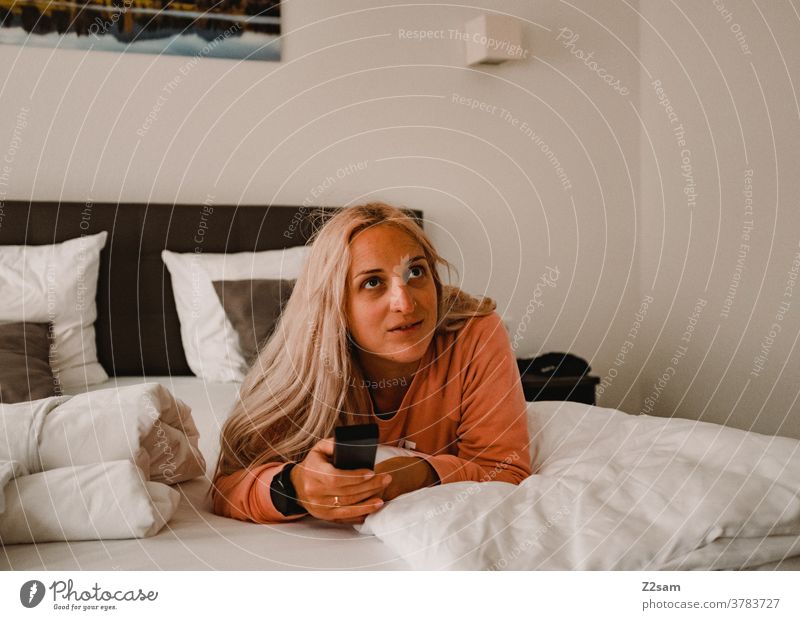 Junge Frau liegt auf dem Bett und zappt durch die Fernsehprogramme Fernsehen fernbedienung junge frau blond lange haare bett entspannung erholung glücklich