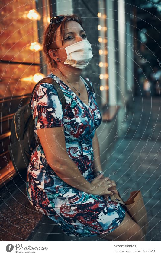 Junge Frau, die nach einem Einkauf im Stadtzentrum im Freien an der Café-Front sitzt und die Gesichtsmaske trägt, um eine Virusinfektion zu vermeiden Kaukasier