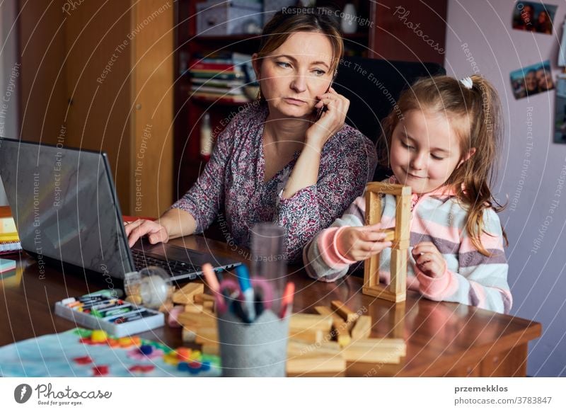 Mutter arbeitet bei der Erledigung ihrer Arbeit aus der Ferne während eines Video-Chat-Call-Stream-Online-Kurses Webinar auf einem Laptop von zu Hause aus, während ihre Tochter mit einem Ziegelsteinspielzeug spielt