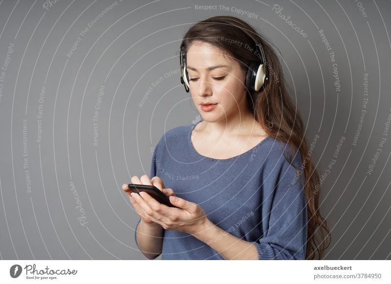 junge Frau, die mit kabellosen Kopfhörern und einem Smartphone Musik hört Bluetooth Mobile Drahtlos Schnurlos Zelle Telefon klug zuhören Mädchen Person Menschen