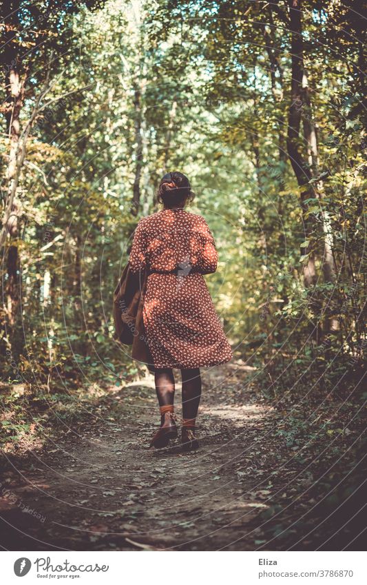 Frau in einem rotweiß gemusterten Kleid geht im Herbst im Wald spazieren. Spaziergang gehen Rückansicht Waldspaziergang Natur alleine Weg Ruhe grün Bäume