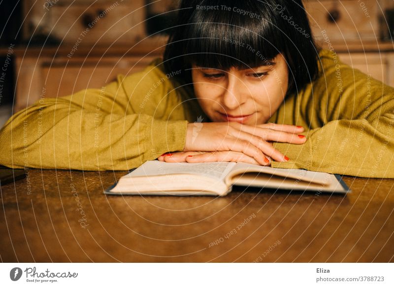 Eine Frau sitzt zuhause am Küchentisch und liest ein Buch lesen Leseratte gemütlich Lesestoff Roman Bildung Literatur vertieft konzentriert Pullover